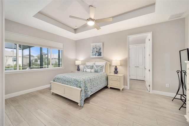 bedroom featuring a raised ceiling, visible vents, light wood-style flooring, and baseboards