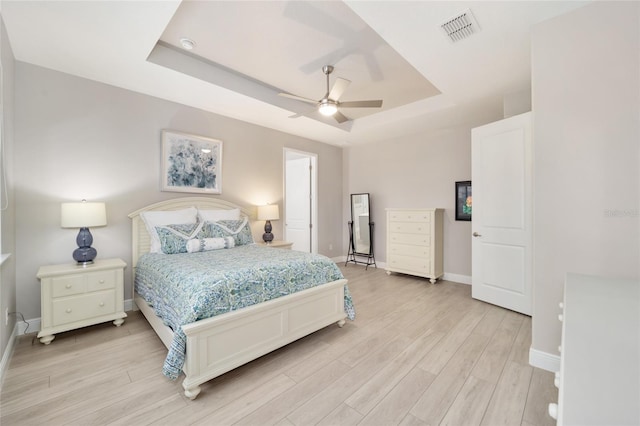 bedroom featuring visible vents, baseboards, a ceiling fan, a tray ceiling, and light wood-style floors