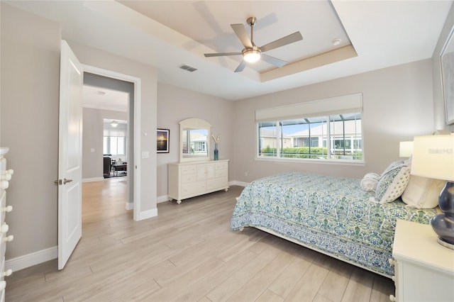 bedroom with ceiling fan, visible vents, baseboards, light wood-style floors, and a raised ceiling