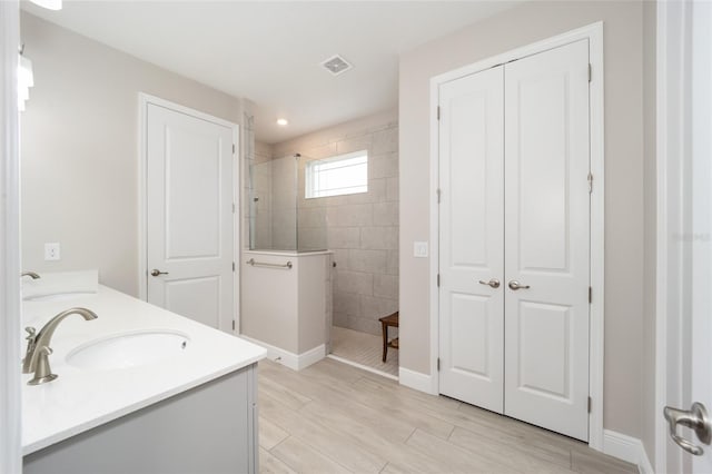 bathroom with wood finish floors, double vanity, visible vents, a sink, and walk in shower