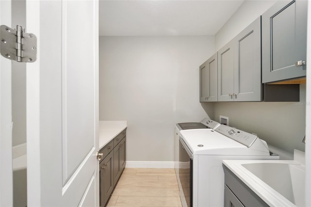 washroom featuring cabinet space, baseboards, washing machine and clothes dryer, light wood-style floors, and a sink