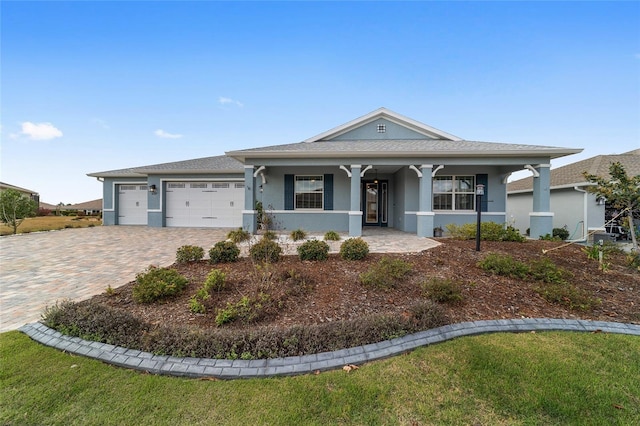 view of front of house featuring decorative driveway, stucco siding, covered porch, an attached garage, and a front lawn