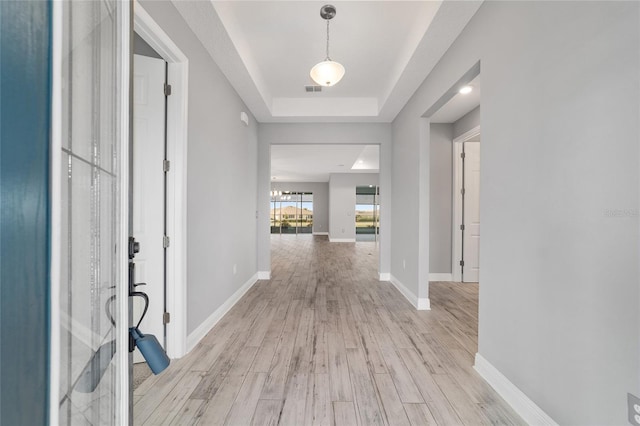 corridor featuring light wood-style floors, visible vents, baseboards, and a raised ceiling