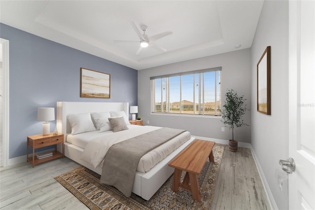 bedroom featuring ceiling fan, a tray ceiling, light wood-type flooring, and baseboards