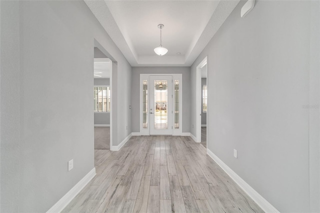 foyer featuring light wood-type flooring, a raised ceiling, and baseboards