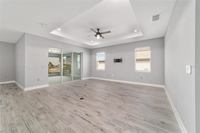 unfurnished room featuring light wood-type flooring, a tray ceiling, visible vents, and baseboards