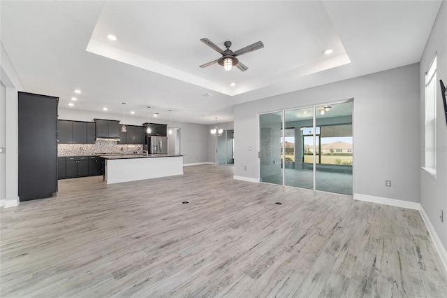 unfurnished living room with light wood-style floors, baseboards, a tray ceiling, and ceiling fan with notable chandelier