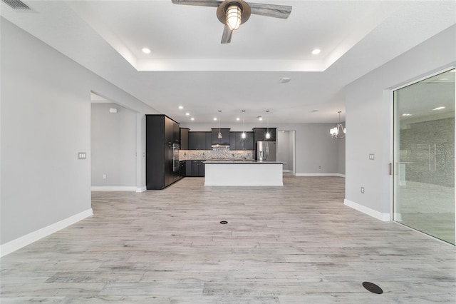 unfurnished living room featuring light wood-style flooring, baseboards, a raised ceiling, and ceiling fan with notable chandelier