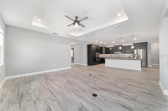 unfurnished living room with visible vents, a tray ceiling, ceiling fan, and baseboards