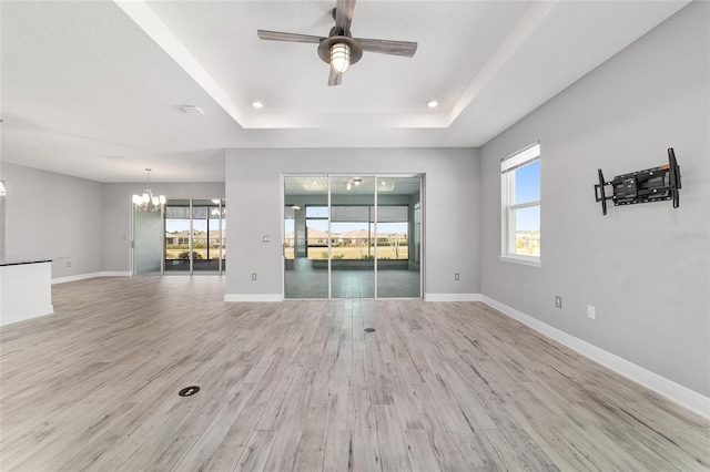 spare room featuring a tray ceiling, light wood finished floors, and baseboards