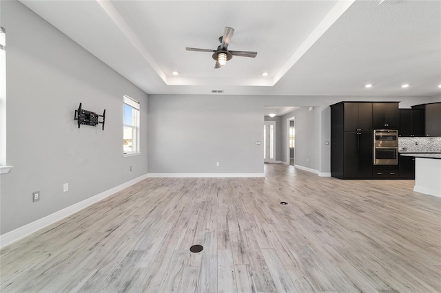 unfurnished living room featuring light wood-type flooring, a raised ceiling, plenty of natural light, and baseboards