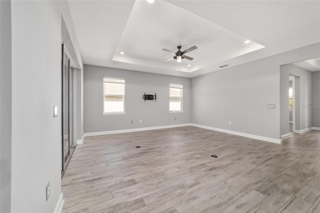 unfurnished room featuring a raised ceiling, visible vents, light wood-style floors, a ceiling fan, and baseboards