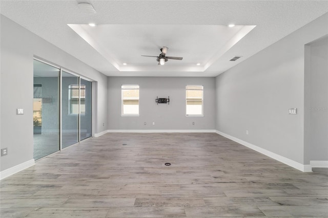 unfurnished room featuring ceiling fan, wood finished floors, visible vents, baseboards, and a tray ceiling