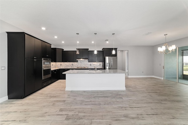 kitchen featuring stainless steel appliances, dark cabinetry, backsplash, an island with sink, and pendant lighting