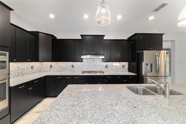 kitchen with appliances with stainless steel finishes, pendant lighting, dark cabinets, and light countertops