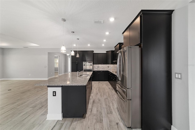 kitchen featuring visible vents, a kitchen island with sink, stainless steel appliances, pendant lighting, and a sink