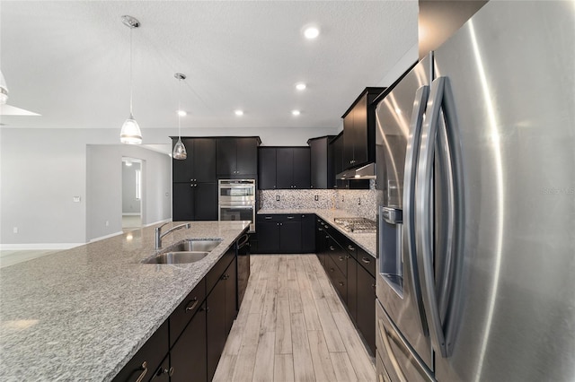 kitchen with pendant lighting, stainless steel appliances, decorative backsplash, a sink, and dark cabinets