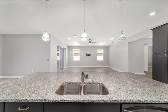 kitchen featuring a kitchen island with sink, a sink, open floor plan, light stone countertops, and decorative light fixtures