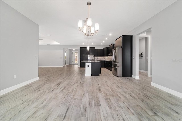 kitchen with a kitchen island with sink, open floor plan, light countertops, freestanding refrigerator, and pendant lighting