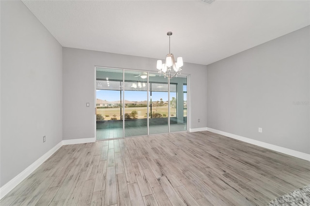 spare room with light wood-style floors, a chandelier, and baseboards