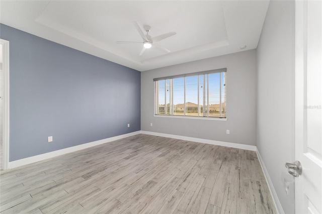 unfurnished room featuring baseboards, a tray ceiling, a ceiling fan, and light wood-style floors