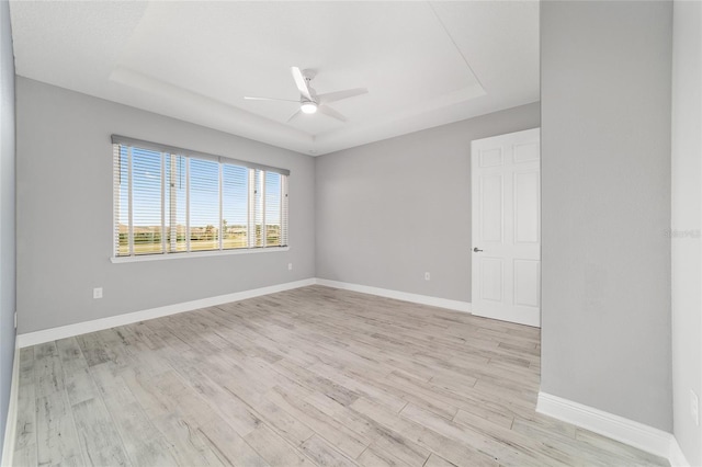 empty room with light wood-style floors, baseboards, a raised ceiling, and a ceiling fan