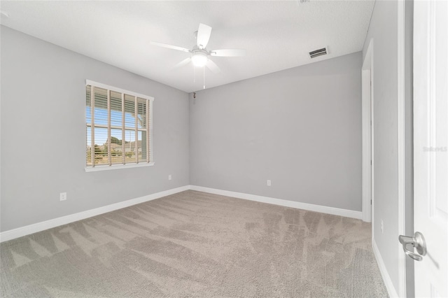 carpeted spare room with visible vents, baseboards, and a ceiling fan