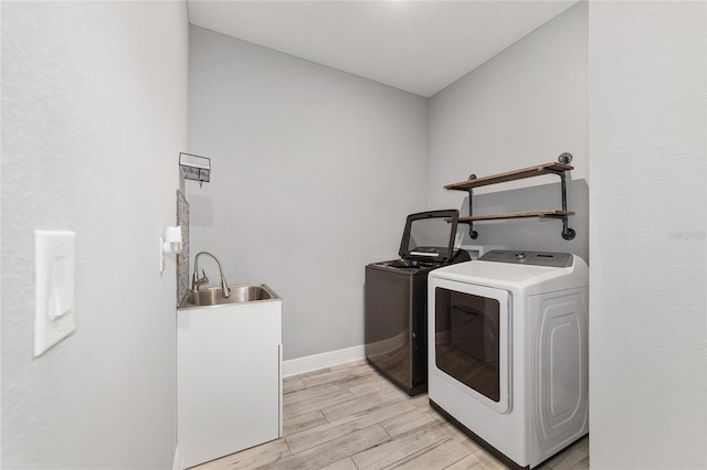 laundry room featuring laundry area, baseboards, wood finish floors, washing machine and dryer, and a sink