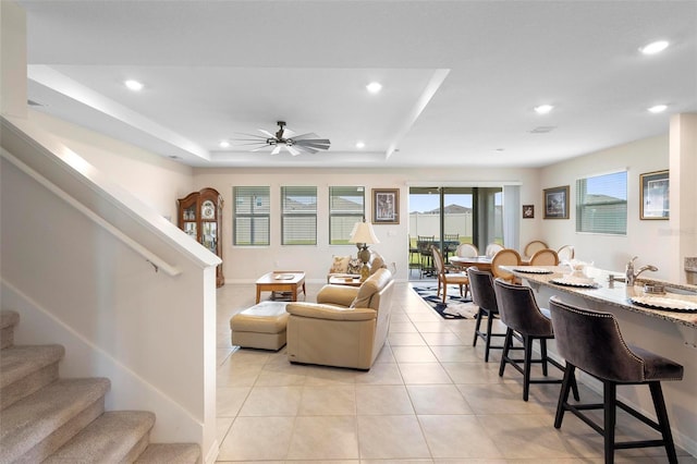 living room with light tile patterned floors, ceiling fan, recessed lighting, stairway, and a tray ceiling