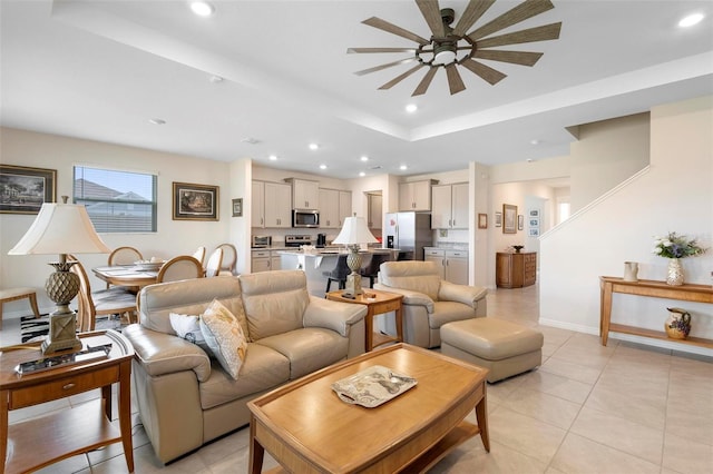 living room with recessed lighting, baseboards, ceiling fan, a tray ceiling, and light tile patterned flooring