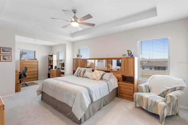 bedroom featuring a raised ceiling, light colored carpet, ceiling fan, and baseboards