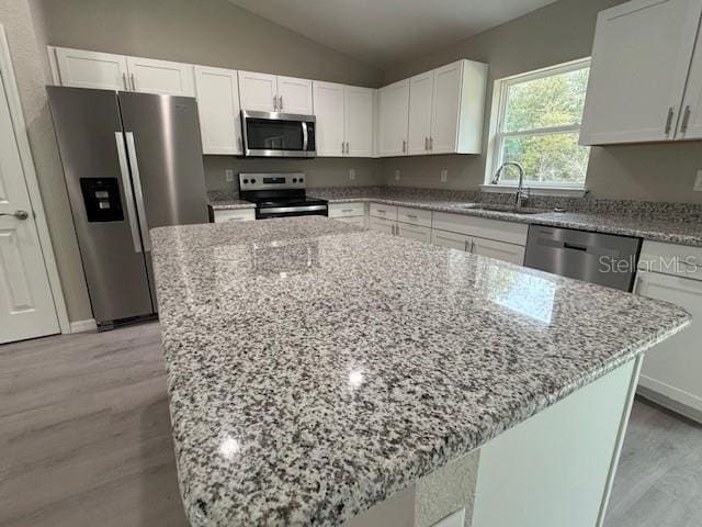 kitchen with a sink, stainless steel appliances, light stone countertops, and white cabinetry