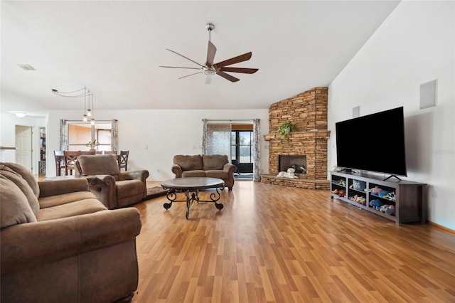 living room with ceiling fan, a stone fireplace, high vaulted ceiling, and light hardwood / wood-style flooring