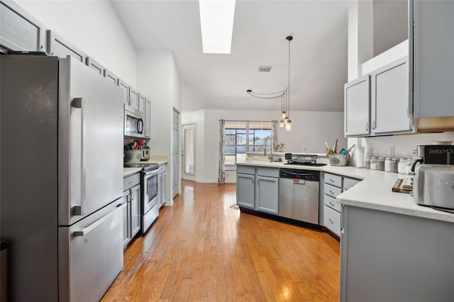 kitchen with light hardwood / wood-style flooring, gray cabinets, appliances with stainless steel finishes, decorative light fixtures, and kitchen peninsula