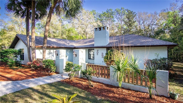 ranch-style home with a shingled roof, a chimney, and stucco siding