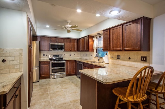 kitchen with appliances with stainless steel finishes, a ceiling fan, a sink, a peninsula, and a kitchen bar