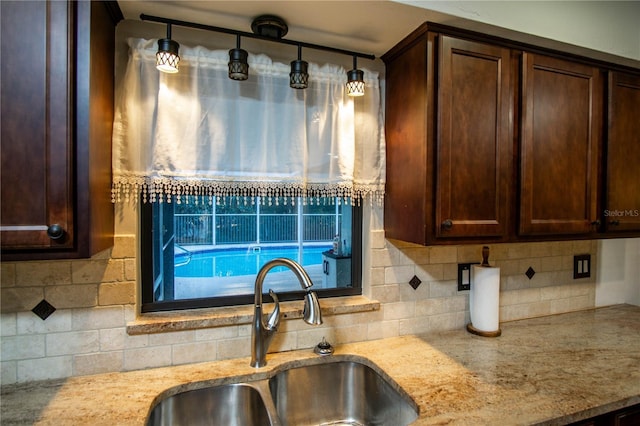 kitchen featuring decorative backsplash, a sink, dark brown cabinetry, and light stone countertops