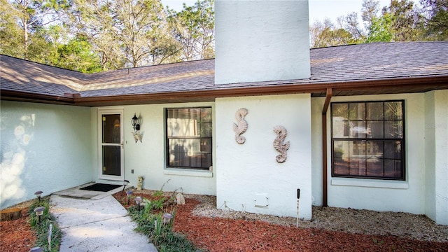 property entrance featuring a shingled roof, crawl space, a chimney, and stucco siding