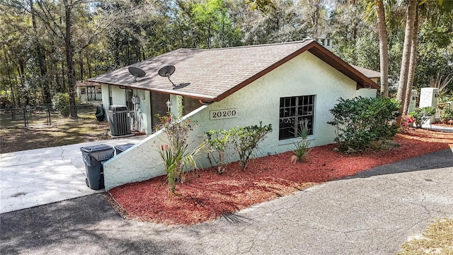 view of front of house with roof with shingles, fence, and stucco siding