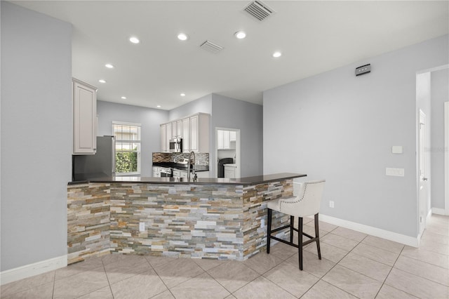 kitchen featuring tasteful backsplash, white cabinetry, a breakfast bar area, kitchen peninsula, and stainless steel appliances