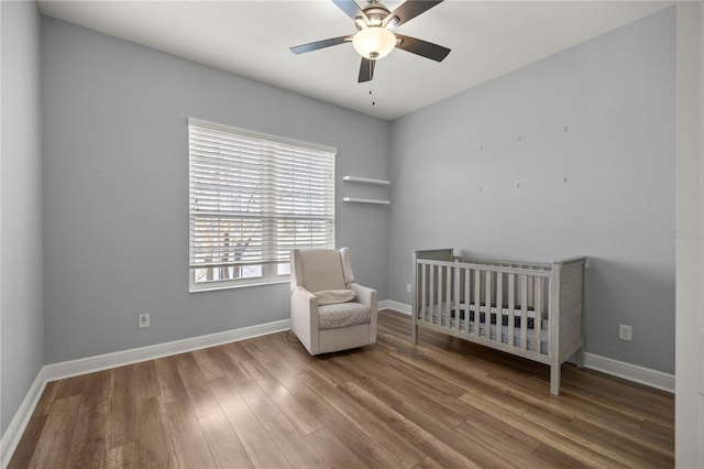 unfurnished bedroom with wood-type flooring, a nursery area, and ceiling fan