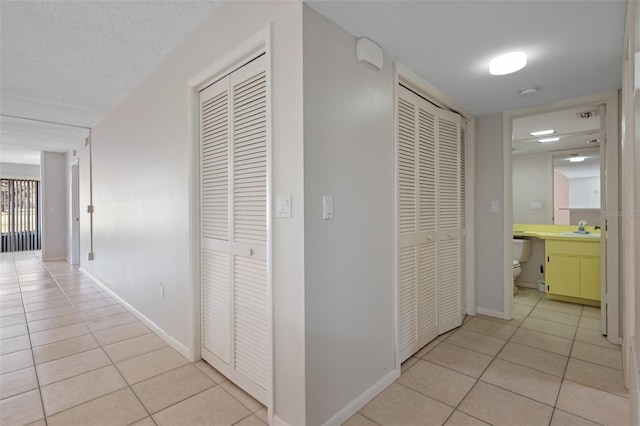 hall with sink, a textured ceiling, and light tile patterned floors