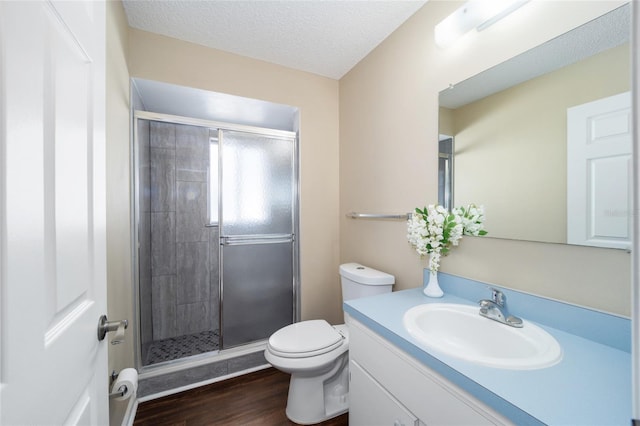 bathroom with wood-type flooring, vanity, toilet, a shower with door, and a textured ceiling