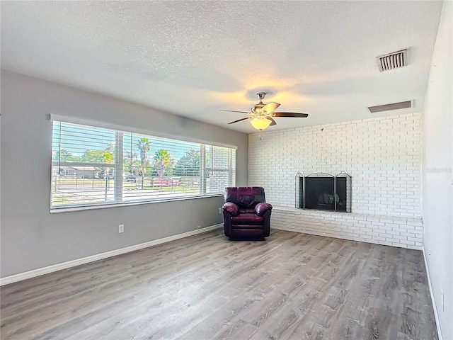 unfurnished room with ceiling fan, a fireplace, a textured ceiling, and light wood-type flooring