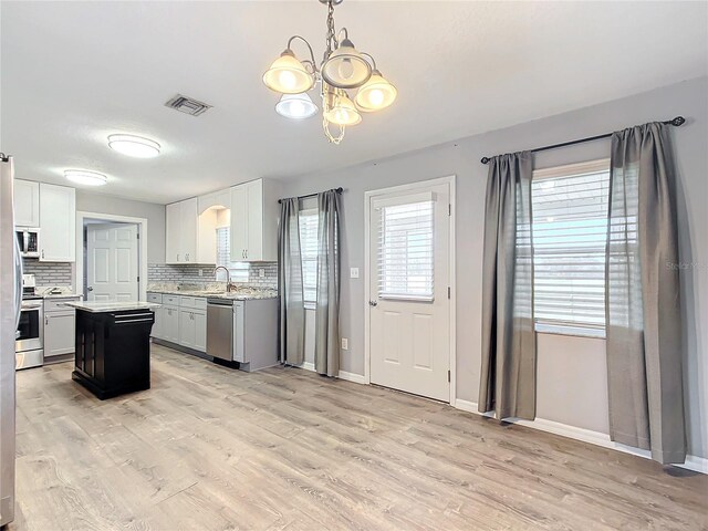 kitchen featuring a kitchen island, appliances with stainless steel finishes, white cabinetry, decorative backsplash, and light wood-type flooring