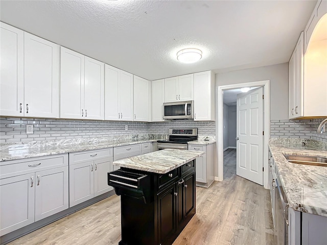 kitchen featuring white cabinetry, sink, light stone counters, stainless steel appliances, and light hardwood / wood-style flooring