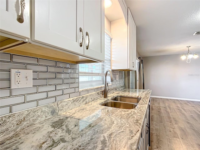 kitchen featuring sink, backsplash, light stone countertops, white cabinets, and light wood-type flooring