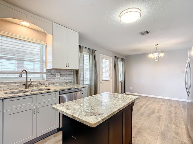 kitchen featuring sink, backsplash, a center island, light stone counters, and decorative light fixtures