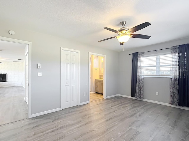 unfurnished bedroom featuring ensuite bath, light wood-type flooring, ceiling fan, a textured ceiling, and a closet
