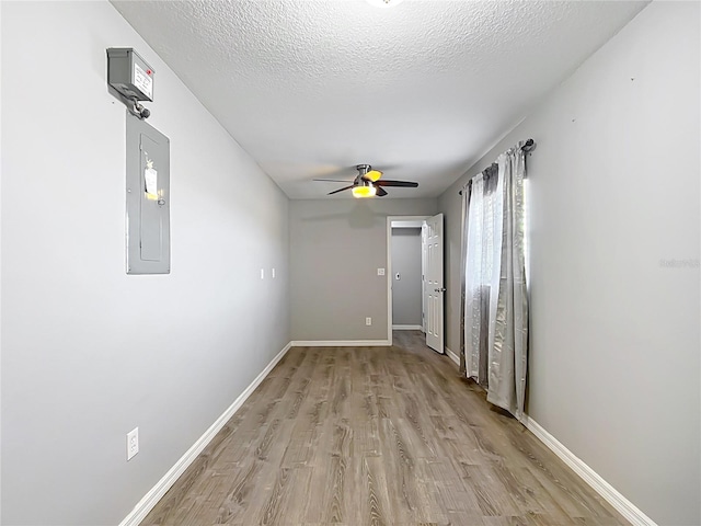 hallway with electric panel, a textured ceiling, and light wood-type flooring